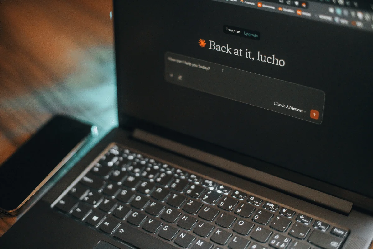 A laptop displays a dark-themed chat interface with text “Back at it, lucho.”